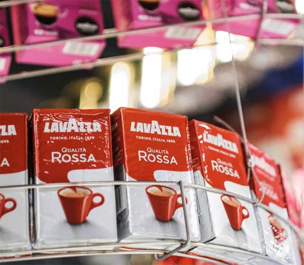 Lavazzaの歴史  すべては1895年に、ルイージ・ラヴァッツァ(Luigi Lavazza)がトリノのサン・トンマーゾ通りに初めて「ラヴァッツァ雑貨店(Drogheria Lavazza)」を開いたことから始まりました。ルイージ・ラヴァッツァは、革新精神にあふれ、創造性と仕事への情熱を持った人物でした。  ラヴァッツァのブレンドが誕生した経緯 ルイージは、さまざまなコーヒー豆の起源や特徴を見出し、それらをブレンドする技術を磨き、顧客の好みに応えるコーヒーを作り上げました。ブラジルへの旅を通じて、彼は大きな変革の時代に、コーヒーの可能性を見抜きました。今日私たちが飲んでいるラヴァッツァのコーヒーは、ルイージがさまざまな地域からのコーヒー豆を組み合わせて生み出したものです。  1927年：小さな店から企業へ ルイージ・ラヴァッツァは、妻エミリア(Emilia)と子供たちと共に会社を設立しました。当時、会社の資本金は150万リラでした。 この時期、ラヴァッツァは香りを保つために「ペルガミン(Pergamin)」という二重層の紙包装を導入し、家庭向けに大量のコーヒーを販売するための最初のステップを踏み出しました。  1947年 – 戦後の復興 ラヴァッツァは第二次世界大戦とコーヒー禁輸措置を乗り越えました。1947年には、ミラノの「エアロスタジオ・ボルギ(Aerostudio Borghi)」によって、最初のラヴァッツァのロゴが作られ、中心の「A」が今でも象徴的なデザインとなっています。  1955年 – 伝説の「ラヴァッツァ・ブレンド(Miscela Lavazza)」の誕生 1955年、ベッペの息子であるエミリオ・ラヴァッツァが会社に入り、伝説の「ラヴァッツァ・ブレンド」を生み出しました。「ラヴァッツァ、カップの中の楽園(Lavazza Paradiso in tazza)」という最初のスローガンが新聞やラジオで広まりました。  1957年 – イタリア最大のコーヒー企業へ イタリアの経済成長とともに、ラヴァッツァはイタリア最大のコーヒー企業となり、ヨーロッパでのリーダーシップへの道を歩み始めました。  1965年 – 製造工場新設 Lavazzaはトリノ郊外のセッティモ・トリネーゼ地区に新しい製造工場を設立し、これがヨーロッパ最大級のコーヒー焙煎・製造施設となりました。  1971年 – イノベーションで危機を克服 1970年代の経済不況期に、ラヴァッツァは新しい真空包装を導入し、クオリタ・ロッサ(Qualità Rossa)のブレンドを発売しました。1977年には、ニーノ・マンフレディ(Nino Manfredi)が16年間にわたりラヴァッツァの顔となりました。 「もっと飲めば、もっと元気になる(Più lo mandi giù e più ti tira su)」や「コーヒーは喜び、良くなければ何の喜びでもない(Il caffè è un piacere, se non è buono che piacere è?)」といった名セリフで、ブランドの認知度をさらに高めました。しかし、マンフレディはLavazzaのすべての商品を宣伝していたわけではありません。たとえば「Paulista」コーヒーは、夫婦として知られるライモンド・ヴィアネッロとサンドラ・モンダイーニが宣伝し、デカフェの「Lavazza Dek」は1988年に特別な広告が放送されました。デカフェとは、カフェインを含まない、もしくはカフェインの量を極力減らしたコーヒーのことを指します。日本ではまだあまり馴染みがないかもしれませんが、カフェインを控えたい方や、夜遅い時間にもコーヒーを楽しみたい方に向けて欧米では人気があります。Lavazzaのデカフェ商品は、通常のコーヒーと同じく豊かな味わいが特徴です。  1980年代 – 世界進出を果たす ラヴァッツァは1980年代に国際展開を始め、フランス、ドイツ、オーストリア、アメリカ、イギリスに拠点を開設しました。広告も国際的に広がり、イタリアらしい高品質なコーヒーの魅力を伝えました。  1989年 – バリスタの育成 「トレーニングセンター ラヴァッツァ(Training Center Lavazza)」を設立し、バリスタの育成や新製品の研究開発を行う拠点としました。  1990年代 – ラヴァッツァの新たな表現  1995年、エミリオ・ラヴァッツァ(Emilio Lavazza)とアルマンド・テスタ(Armando Testa)との協力で、5代目のラヴァッツァのロゴが誕生しました。また、有名シェフとの協力を始め、象徴的な「ラヴァッツァカレンダー(Calendario Lavazza)」も生まれました。  2004年 – 社会的責任への取り組み 2004年、ラヴァッツァは持続可能性を目指し、「¡ティエッラ！(¡Tierra!)」プロジェクトを開始しました。このプロジェクトを通じて、世界中のコーヒー農家の生活条件を改善し、新しい持続可能な農業技術を導入しました。]  2005年には、カバジェロ(Caballero)とカルメンシータ(Carmencita)が再び広告に登場しました。この時、イタリアのテレビ局「イタリア1（Italia 1）」でミニシリーズとして放送されました。イタリア1は、バラエティ、ドラマ、アニメなどを放送するイタリアの主要な民放テレビ局で、特に若年層に人気があります。このミニシリーズは、過去の人気キャラクターに新たな命を吹き込む試みとして話題を呼びました。  Lavazzaの革新は技術面にも及び、2015年には、国際宇宙ステーションのために「ISSpresso」マシンを開発。イタリアの宇宙飛行士サマンサ・クリストフォレッティ(Samantha Cristoforetti)がこのマシンを使用し、宇宙空間でのコーヒー体験を提供しました。  トリノのボルゴ・アウローラ(Borgo Aurora)地区に「Nuvola Lavazza」という新しい本社を設立。これにはLavazzaの歴史やコーヒー文化を紹介する博物館(Museo Lavazza)も併設されています。Lavazzaは、伝統を守りつつも常に革新を続ける、世界的なコーヒーブランドとして成長を続けています。  また、Lavazzaの海外広告キャンペーンでは、著名な写真家を起用していることでも知られています。ジャン＝バティスト・モンディーノ、デヴィッド・ラシャペル、ヘルムート・ニュートン、アルバート・ワトソン、アニー・リーボヴィッツなどの著名なアーティストが手掛けた作品が、Lavazzaの国際的な広告キャンペーンを飾り、Lavazzaカレンダーでもその芸術的な価値が高く評価されています。さらに、Lavazzaは2020年のF1世界選手権でウィリアムズF1の公式パートナーにもなりました。